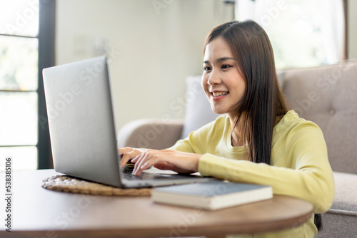 Young woman is sitting to smiling on the floor and using laptop to typing business report while working