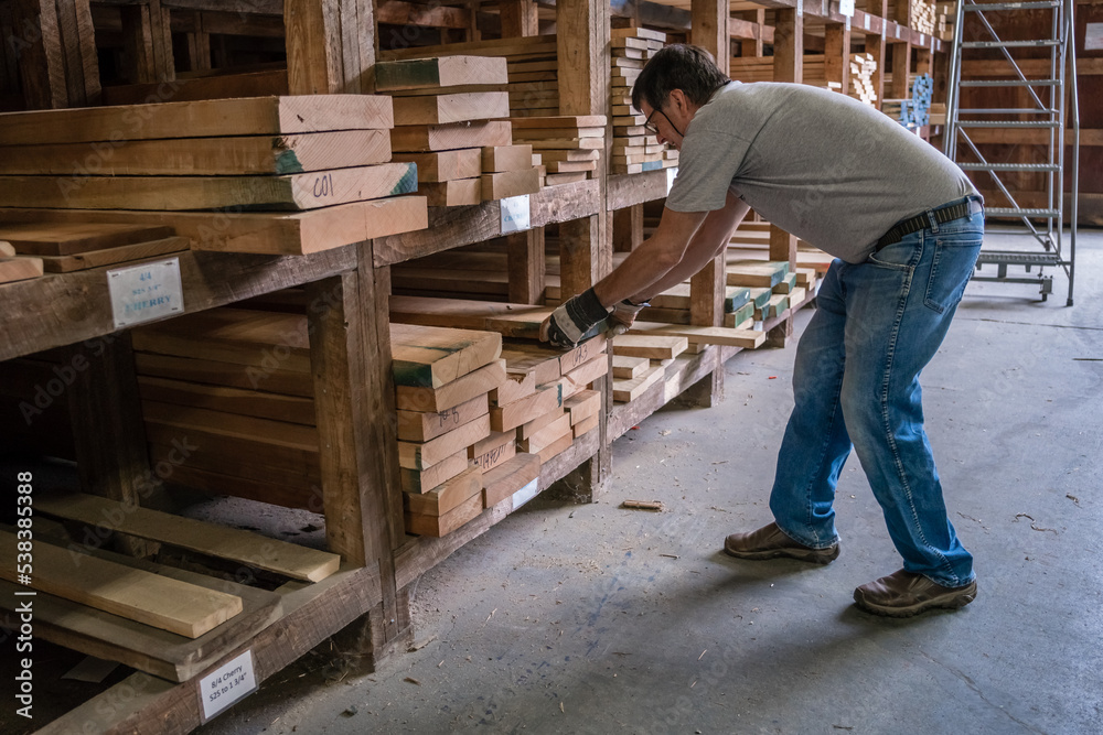Kingston, NH, US-September 12, 2022: Man choosing lumber in local lumber yard with stacks of hardwoods and softwoods in background. Kingston, NH, US-September 12, 2022: Man choosing lumber in local lumber yard with stacks of hardwoods and softwoods in background.