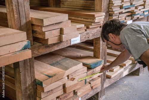 Kingston, NH, US-September 12, 2022: Man choosing lumber in local lumber yard with stacks of hardwoods and softwoods in background. photo