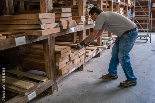 Kingston, NH, US-September 12, 2022: Man choosing lumber in local lumber yard with stacks of hardwoods and softwoods in background.