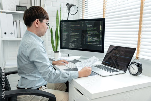 Male programmer is programing to developing program app and website of corporate while working to checking program code and debugging on multiple screen at modern software office