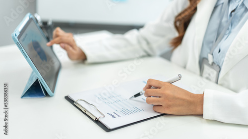 Businesswoman is reading marketing plan report on tablet to taking notes in document and analysis