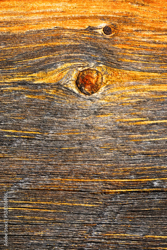 Close-up of a knothole in unfinished, raw, weathered wood, revealing an abstract design in rough textures.