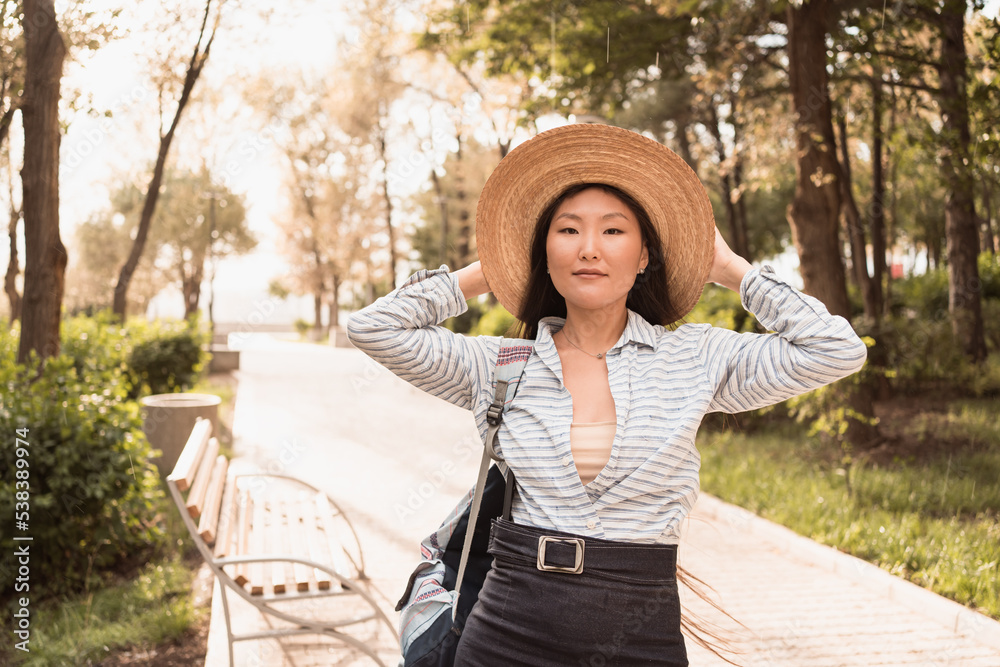 Young asian woman in hat walking in city park in summer