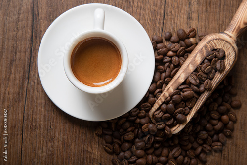 White cup of espresso with coffee beans on wooden background 