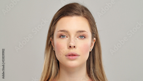 Beautiful young girl looks at the camera after professional makeup. Model poses in front of the camera. An attractive girl with beautiful makeup. Close-up face of a white model with long hair.