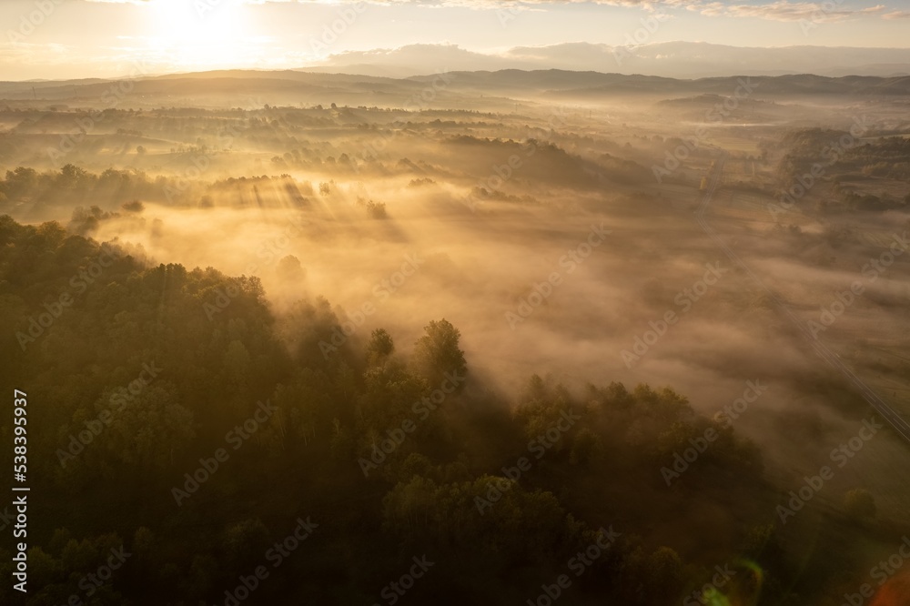 Aerial colorful view of foggy autumn morning over hills and forests, in Soceni village, Romania. Captured from above, with a drone.