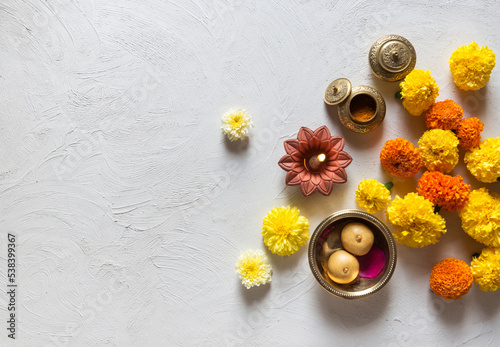 Marigold flowers scattered on white background with Indian traditional lamp, kumkum and sweet. Beautiful Hindu festive background or photo. View from above.