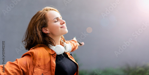 Joyful and satisfied woman with closed eyes in casual clothes and big headphones on her neck, mental wellbeing, happy life. photo