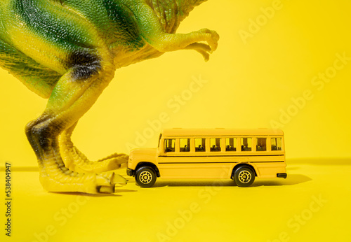 Giant toy tyrannosaurus rex with school bus on a yellow background.