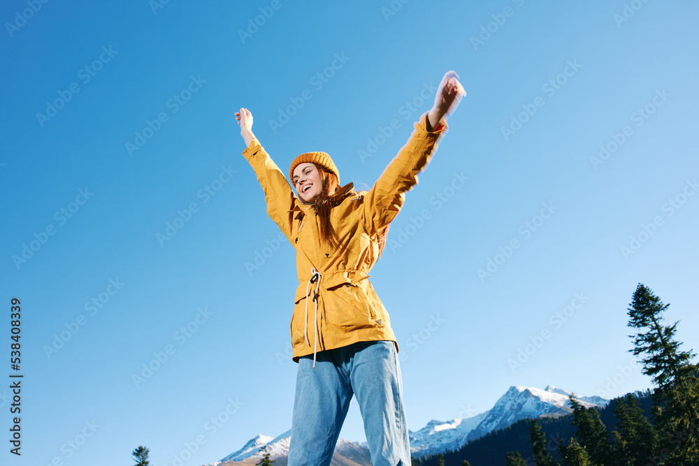 Woman with red hair hiker standing on mountain hands up happiness overlooking snowy mountains in yellow raincoat and cap travel in winter and hiking in the mountains in the sunset freedom Woman with red hair hiker standing on mountain hands up happiness overlooking snowy mountains in yellow raincoat and cap travel in winter and hiking in the mountains in the sunset freedom