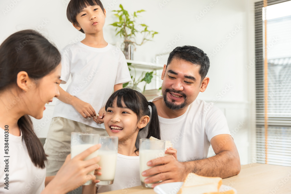 Asian family enjoying breakfast at living room. little girl daughter sitting on table, drinking milk with smiling father and mother in morning. Happy family at home. Asian family enjoying breakfast at living room. little girl daughter sitting on table, drinking milk with smiling father and mother in morning. Happy family at home.