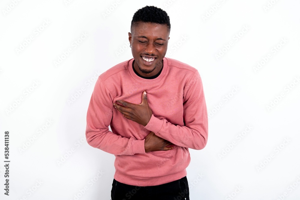 young handsome man wearing pink sweater over white background keeps hands crossed, laughs out loud at good joke, wears casual clothes. young handsome man wearing pink sweater over white background keeps hands crossed, laughs out loud at good joke, wears casual clothes.