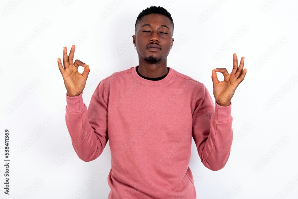 young handsome man wearing pink sweater over white background doing yoga, keeping eyes closed, holding fingers in mudra gesture. Meditation, religion and spiritual practices. young handsome man wearing pink sweater over white background doing yoga, keeping eyes closed, holding fingers in mudra gesture. Meditation, religion and spiritual practices.