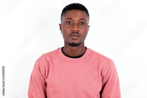 Joyful young handsome man wearing pink sweater over white background looking to the camera, thinking about something. Both arms down, neutral facial expression.