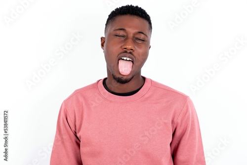 young handsome man wearing pink sweater over white background with happy and funny face smiling and showing tongue.