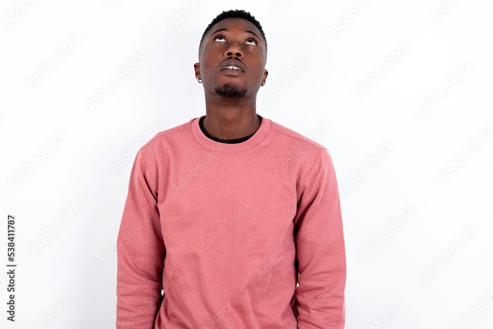 young handsome man wearing pink sweater over white background looking up as he sees something strange. young handsome man wearing pink sweater over white background looking up as he sees something strange.