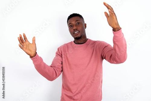 Cheerful young handsome man wearing pink sweater over white background making a welcome gesture raising arms over head.