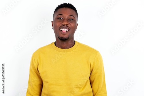 young handsome man wearing yellow sweater over white background with happy and funny face smiling and showing tongue.