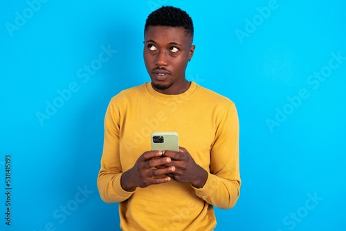 young handsome man wearing yellow T-shirt over blue background holds telephone hands reads good youth news look empty space advert