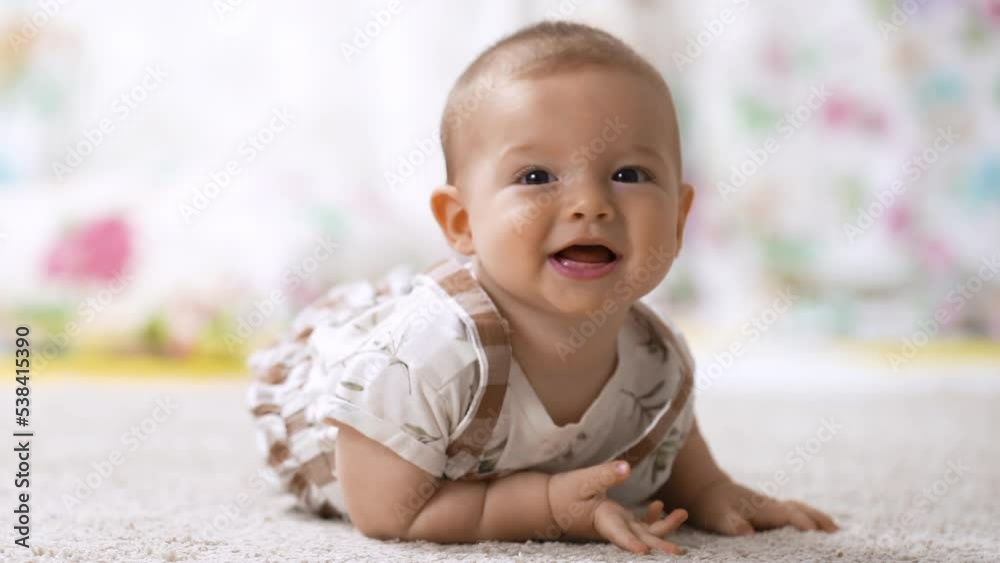 Happy healthy six-month-old baby trying roll over from the back to the stomach for the first time on the floor in the nursery. Healthy growth and development of the child's skills Happy healthy six-month-old baby trying roll over from the back to the stomach for the first time on the floor in the nursery. Healthy growth and development of the child's skills