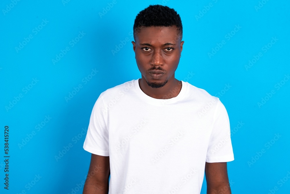 Obraz premium Offended dissatisfied young handsome man wearing white T-shirt over blue background with moody displeased expression at camera being disappointed by something