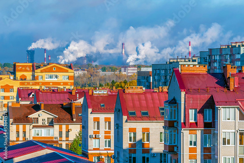 Сityscape - a view of residential apartment buildings in the city against the backdrop of factory pipes emitting toxic smoke into the atmosphere. Problems of heating houses and air pollution.