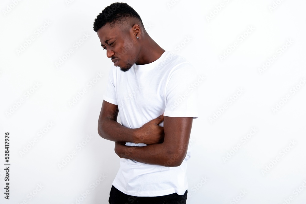 young handsome man wearing white T-shirt over white background got stomachache young handsome man wearing white T-shirt over white background got stomachache