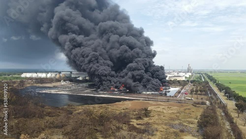 Aerial footage of a large scale Oil refinery with smoke because explosions stacks and petroleum storage tanks. Massive fire explosion or strike in military combat and war.