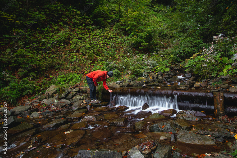 Hiker on a long trail refills drinking water from a mountain spring into a glass container. Replenishing clean water for cooking and drinking while hiking in the wilderness Hiker on a long trail refills drinking water from a mountain spring into a glass container. Replenishing clean water for cooking and drinking while hiking in the wilderness