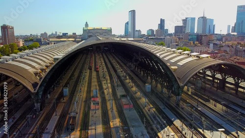 Aerial view of the train station arriving trains. An old wide arched structure made of metal and glass above the station poles. Tourism. Skyline with tall buildings. Italy, Milan, April 2022 photo