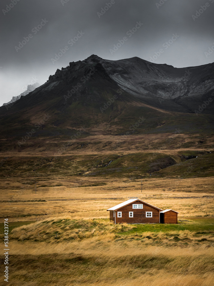 A singled house in an open field in front of mountains shot while traveling through Iceland.