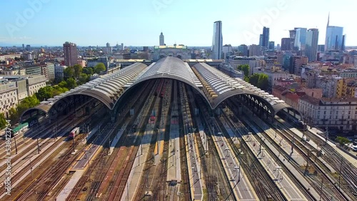 Aerial view of the train station arriving trains. An old wide arched structure made of metal and glass above the station poles. Tourism. Skyline with tall buildings. Italy, Milan, April 2022 photo