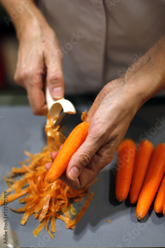 Fotografie manos de cocinera pelando zanahorias con pelador