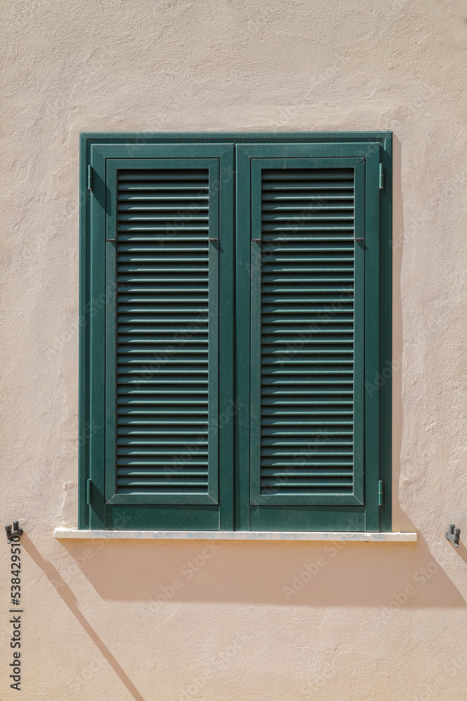 Stone wall with window and closed wooden shutter in green, vertical format Stone wall with window and closed wooden shutter in green, vertical format
