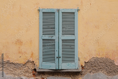 old wooden window on the wall of a house,
closed shutter and damaged wall with cracked surface, 
