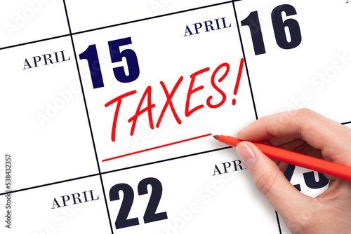 Hand drawing red line and writing the text Taxes on calendar date April 15. Remind date of tax payment