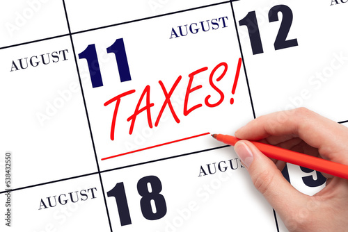 Hand drawing red line and writing the text Taxes on calendar date August 11. Remind date of tax payment