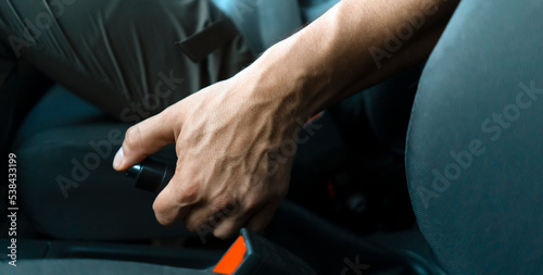 Male hand with handbrake inside the car, closeup view.