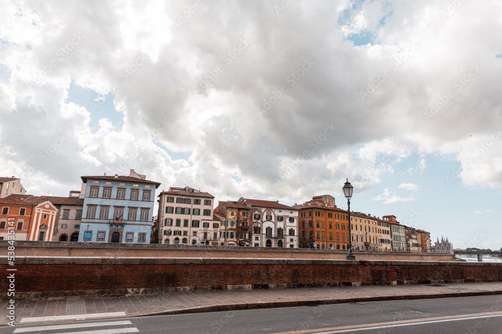 Beautiful cozy European town with vintage houses along the river on a bridge with a cloudy sky. Journey to Pisa, Italy