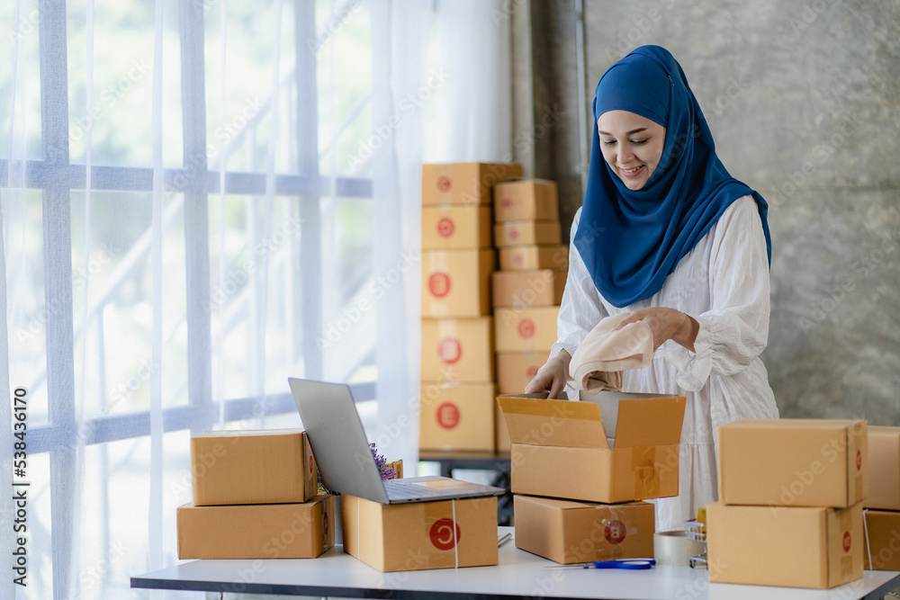 Islamic women selling online at home with boxes beautiful asian woman working at home Selling online with yellow box and laptop to accept orders from customers. SME business idea. Parcel delivery. Islamic women selling online at home with boxes beautiful asian woman working at home Selling online with yellow box and laptop to accept orders from customers. SME business idea. Parcel delivery.