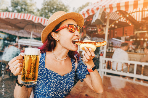 Obraz na płótnie Happy girl drinking beer and eating traditional german bratwurst - hotdog at funfair and street food festival. National cuisine and biergarten concept w salonie