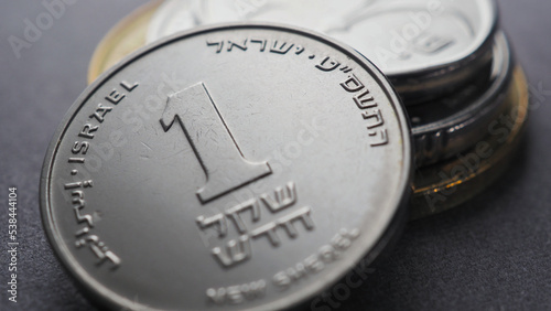 Translation: 1 new shekel Israel. Israeli money. 1 one shekel coin and a stack of other coins. National currency. Close up. Illustration for news about salary or taxes. Macro