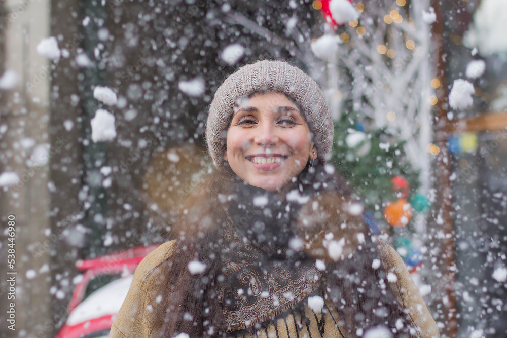 Portrait of a happy pretty girl during Christmas holidays in a festive town at a Christmas fair under snowfall