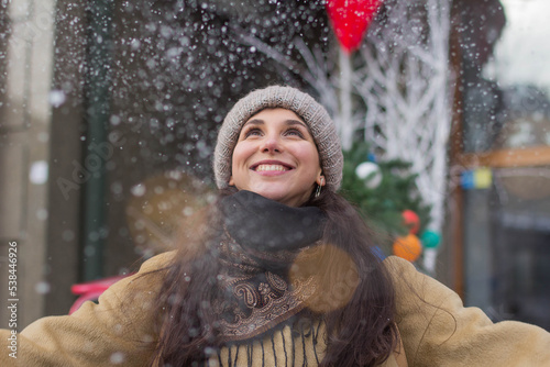 Portrait of a happy pretty girl during Christmas holidays in a festive town at a Christmas fair under snowfall