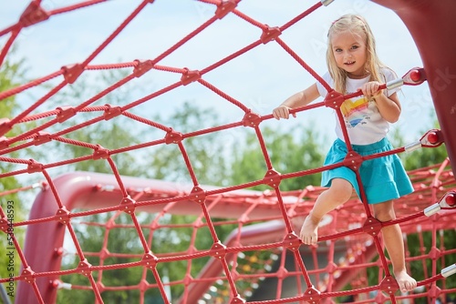A girl climbs a rope attraction in the park. Entertainment for children.