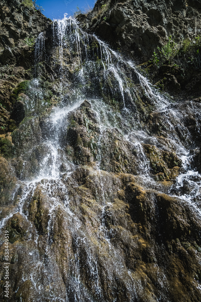 Thin streams of a cold mountain waterfall cascade down the rocks of the mountain, on a warm autumn day Thin streams of a cold mountain waterfall cascade down the rocks of the mountain, on a warm autumn day