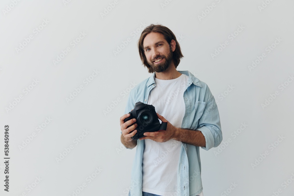 Obraz premium Man hipster photographer in a studio against a white background holding a professional camera and setting it up before shooting. Lifestyle work as a freelance photographer