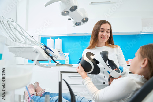 Pediatric dentist preparing kid for teeth check-up using modern technology