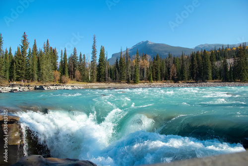 Blue waters of Athabasca waterfalls among forest and mountains.